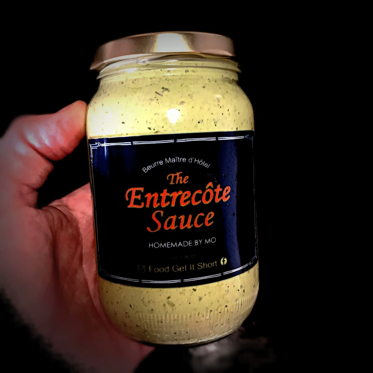 A hand holding a jar of The Entrecôte Sauce